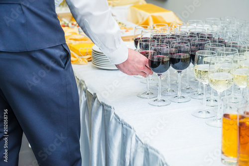 The waiter is servering catering buffet table with alcoholic and non-alcoholic drinks on the business event in the hall. Service at business meeting, party, weddings. Selective focus, space for text. photo