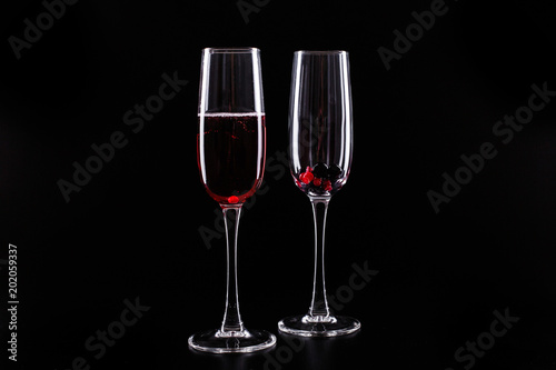 Glass with berries and red champagne alcohol cocktail stands on black background