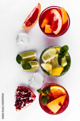 Delicious mojito, rum and cola, blood orange and vodka cocktails served with fruit, mint and ice stand on white table photo