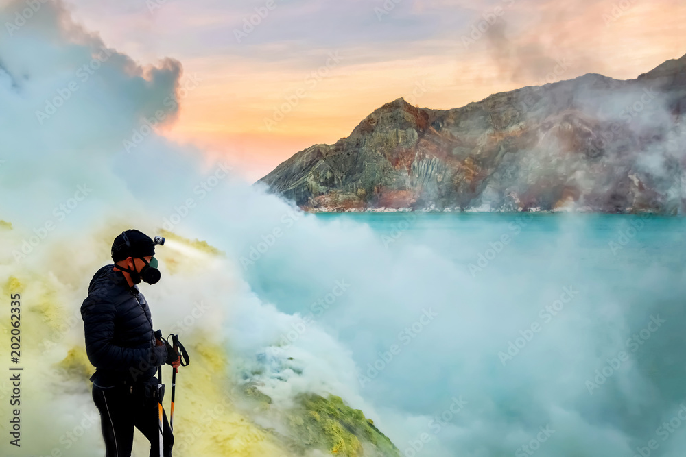 Tourist in the crater of a volcano. Sulfur pairs, volcanic blue lake and pink dawn. A dangerous journey into the mouth of an active volcano. Gunung Ijen. Indonesia. Java island.