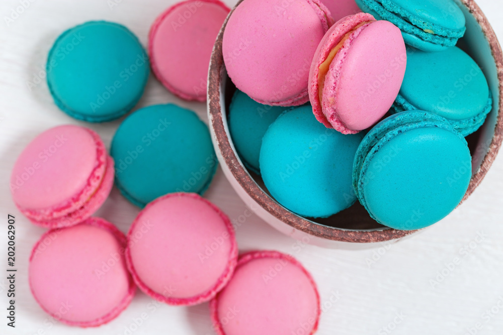 Pink and blue macaroons in bowl on wooden white background with copy space. Food background. Top view. Pink and blue macaroons in bowl on wooden white background with copy space. Food background. Top view.