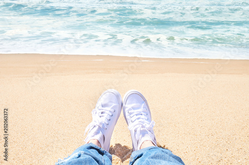 Female feet in jeans and white sneakers on beach. Walk along the beach