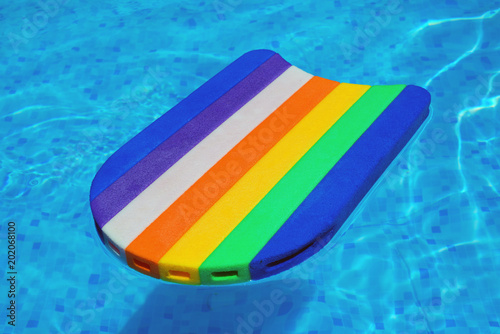 Rainbow pattern styrofoam swimming board baseboard floating in poolside water