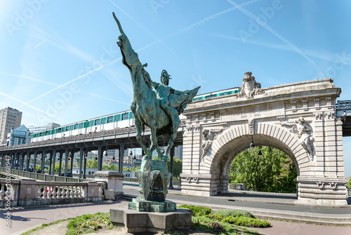 A low angle cinematic view of the France Reborn Statue and landmark as a train rides by, near the Pont de Bir-Hakeim Bridge/Pont De Passy in downtown Paris, France