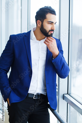 A young successful businessman stands by the window with a conceived expression of the face