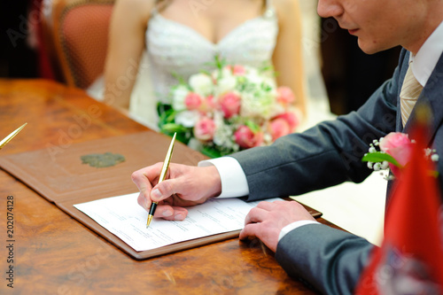 The groom puts his signature in the marriage document.