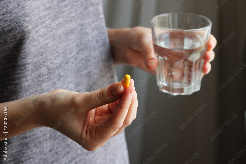 yellow tablet and a glass of water in female hands. Concept of health. yellow tablet and a glass of water in female hands. Concept of health.
