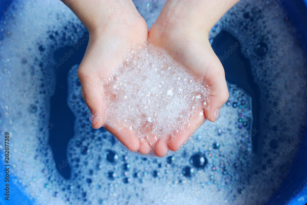 Fototapeta premium soap foam in the hands of the child on a beautiful blue background. Hand hygiene. Children's hygiene.