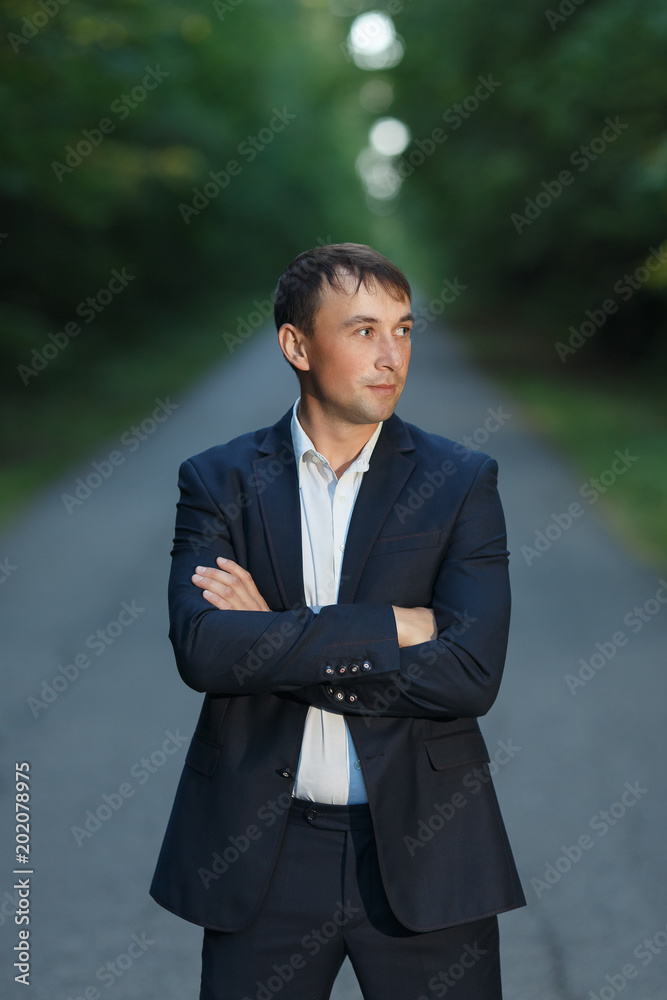 Handsome man in a business suit without a tie on a forest road Handsome man in a business suit without a tie on a forest road