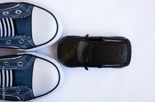 Black model of the SUV car in front of blue sneakers close up on white background