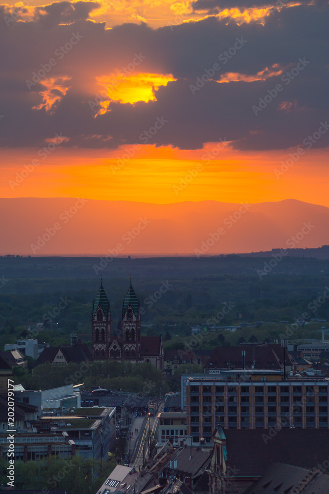 Germany, City Freiburg im Breisgau aerial view on church and city railway with burning orange sunset sky