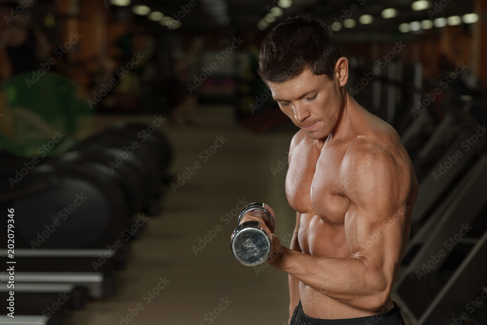 Tanned muscular man workout with dumbbells in gym