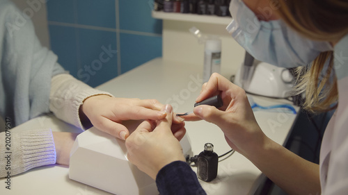 Nail care in the salon. Master applies gel-lacquer on the nails of a young woman