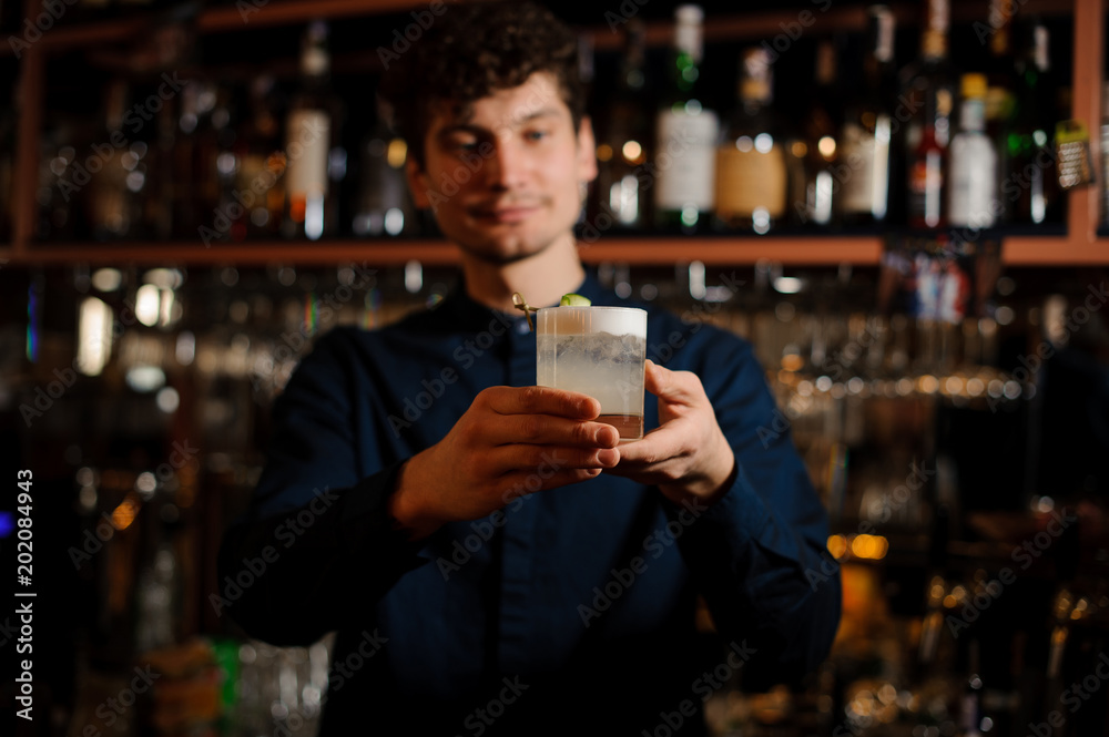 Young curly barman holding a glass with fresh and sour summer cocktail Young curly barman holding a glass with fresh and sour summer cocktail