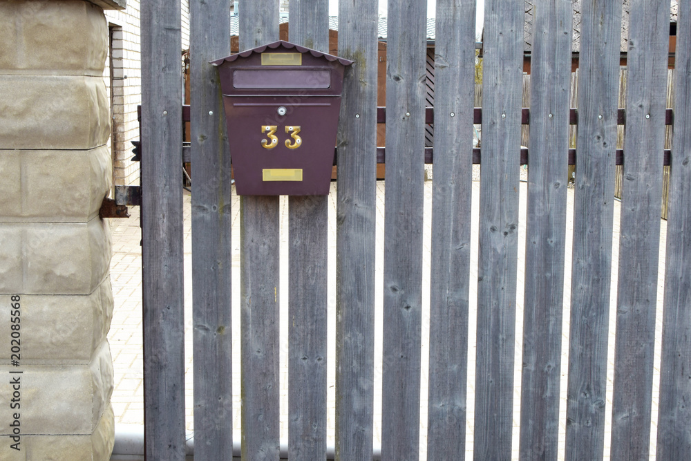 Brown metal mailbox on grey  natural aged wooden fence.