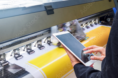 Technician touch control tablet on format inkjet printer during yellow vinyl photo