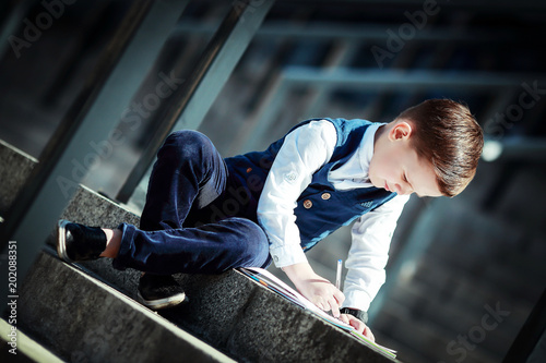 Bild auf Leinwand The younger fashionable boy draws in a notebook sitting on the steps