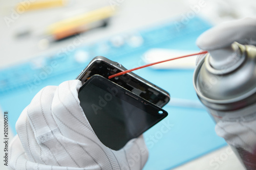 Close up of man's hands dispensing PCB cleaner liquid to remove dirt, dust, contaminants and flux residues from printed circuit board while repairing mobile phone. Electronics and gadgets concept