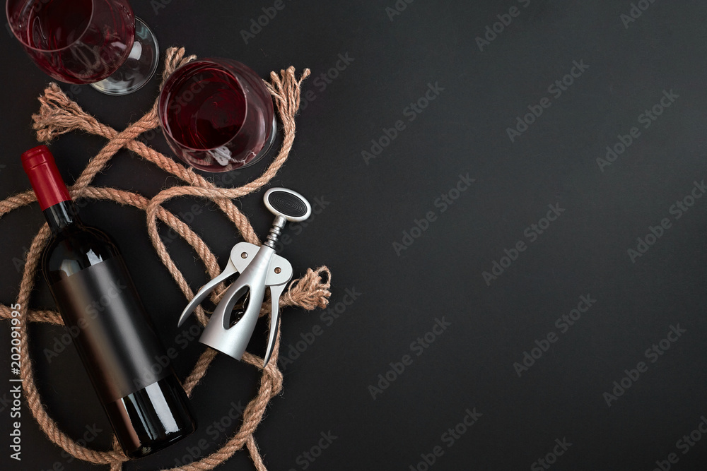 Red wine bottle, two glasses and corkscrew on black background. Top view with copy space