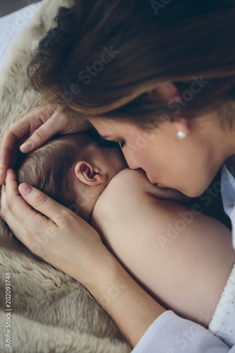 Top view of young mother kissing her newborn baby girl lying on the bed