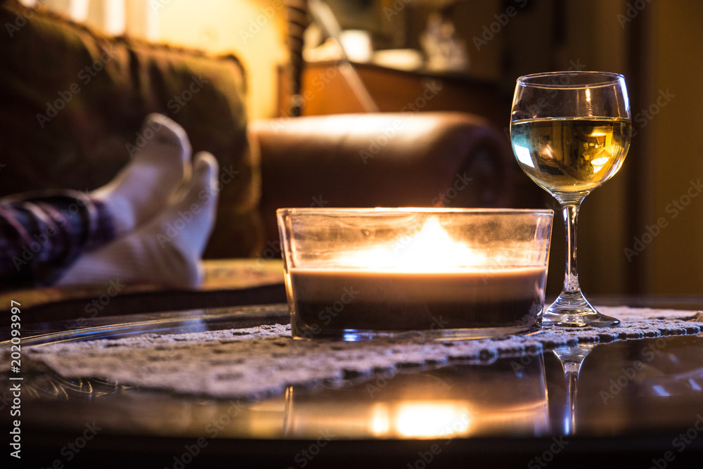 Wine glass and candle in a relaxing scene with persons feet on couch in the background