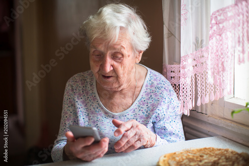 Elderly woman sits with a smartphone in her hands..