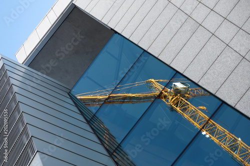 Reflection of construction crane in the blue windows of a building opposite