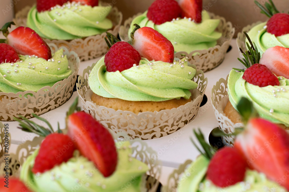 Many green cupcakes with strawberries and raspberries.
