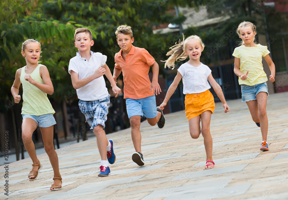 Fototapeta premium Group of cheerful children running together in town on summer