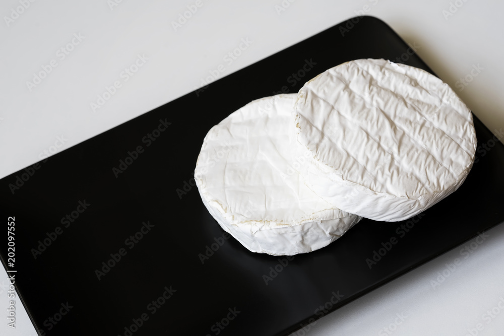 Two heads of camembert or brie cheese in black square plate. Top view. For background, with copy space Two heads of camembert or brie cheese in black square plate. Top view. For background, with copy space