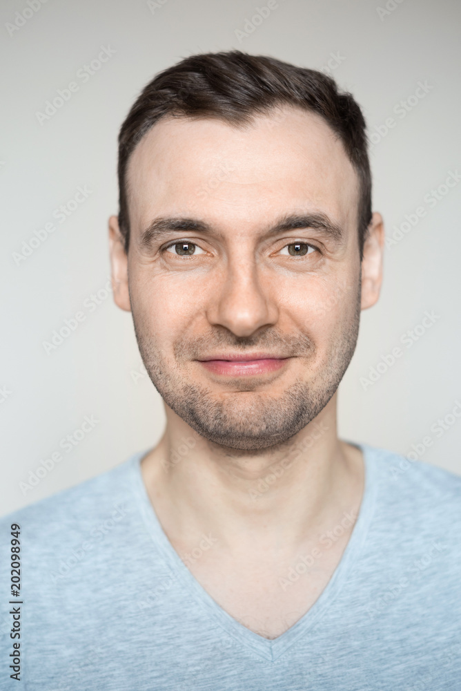 Portrait of a young handsome fashionable guy with a bristle with a smile on his face in a gray shirt on a light background Portrait of a young handsome fashionable guy with a bristle with a smile on his face in a gray shirt on a light background