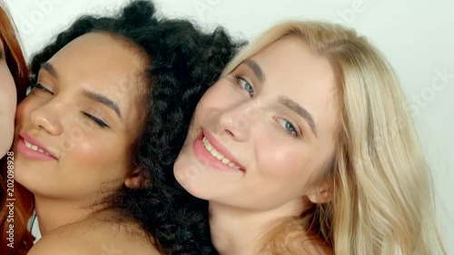 Seductive girl friends with various hair colors are hugging to each other, close-up. Three women are smiling and looking in camera sensually