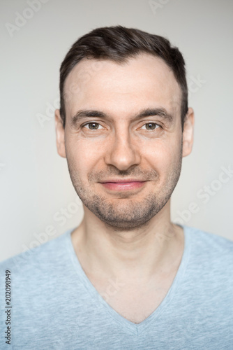 Portrait of a young handsome fashionable guy with a bristle with a smile on his face in a gray shirt on a light background