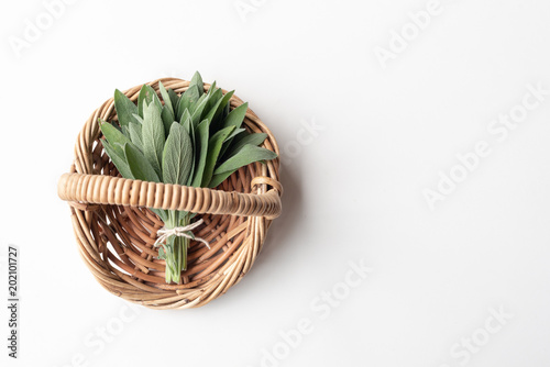 Directly above view of small bunch of sage in wicker basket on white background with copy space  selective focus 