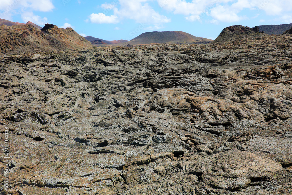 Solidified lava flow and crust with volcanic mountains on the background in Timanfaya National Park, Lanzarote, Canary Islands