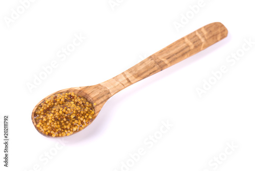 Whole grain Dijon mustard in wooden spoon with brown seeds. Macro food photo close up, isolated on white background.