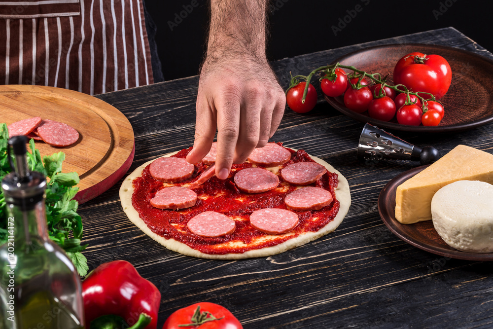 Cook in the kitchen putting the ingredients on the pizza. Pizza concept. Production and delivery of food.
