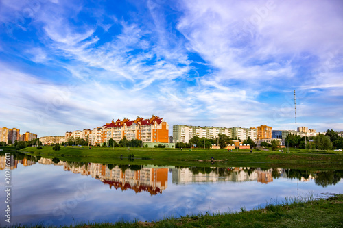 Landscape of the pond on the background of the city on a summer day. Reflection of the sky and buildings in the water 