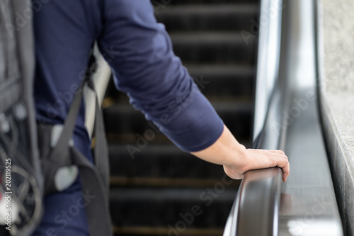 Asian traveller's man holding hand rail go up stairs/floor by escalator to the airport. Backpacker tourist take vacation/holiday on journey alone concept. Bag on male's back hipster adventure trip.