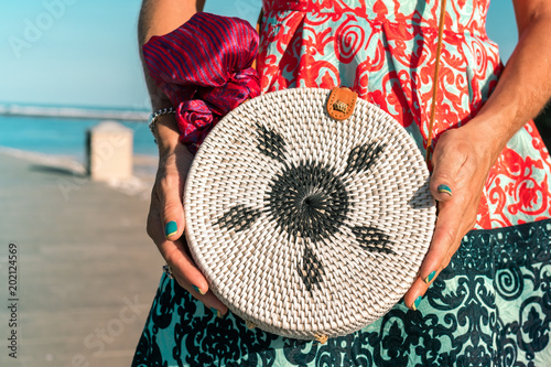 Woman with fashionable stylish rattan bag and silk scarf outside. Tropical island of Bali, Indonesia. Rattan handbag and silk scarf. photo