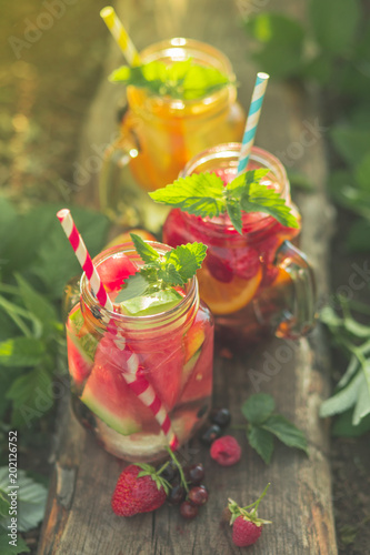 Summer soft drinks with berries and fruits in glass jars, outdoors. Toned image