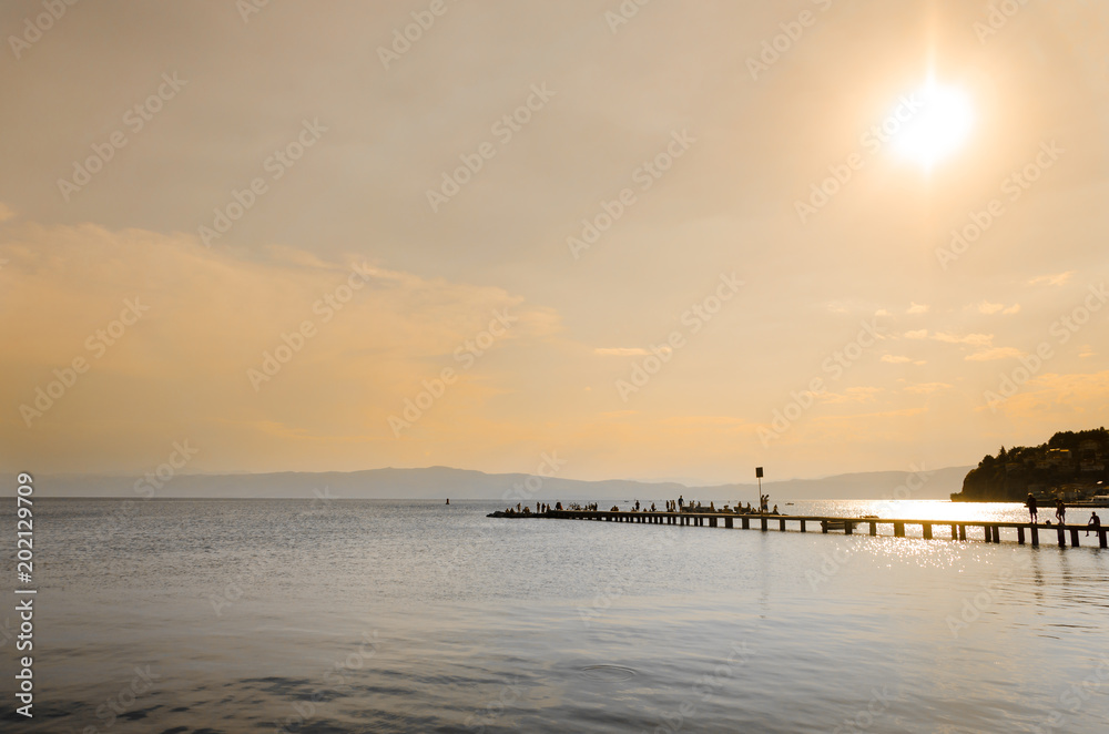 Sunrise or sunset above a boardwalk pier into the water. Warm reflections of the sun and pier on the water