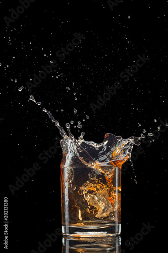 Glass of whiskey with splash isolated on black background