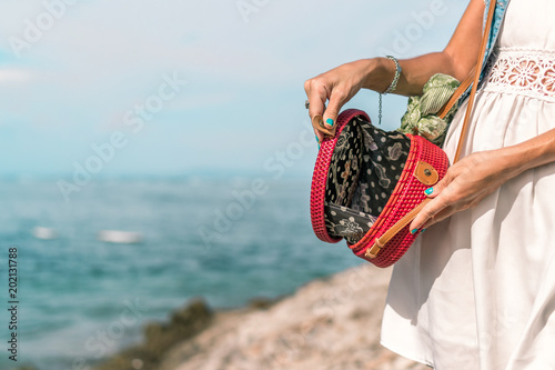 Woman hands with fashionable stylish red rattan bag and silk scarf outside. Tropical island of Bali, Indonesia. Rattan handbag and silk scarf. photo