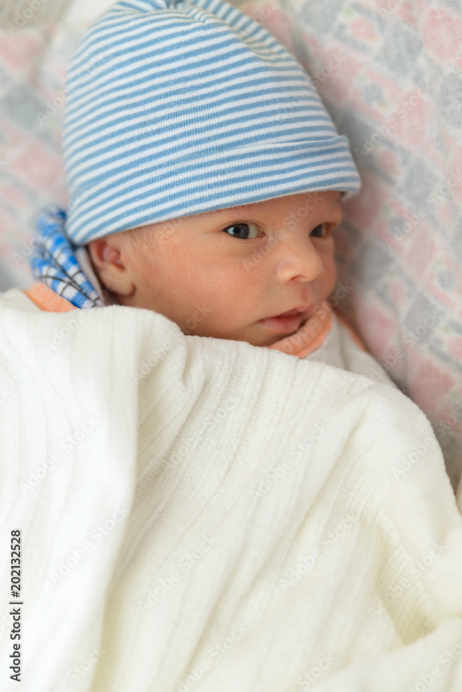 Cute Eurasian newborn baby boy lying on bed and wearing a striped cap  фотография Stock | Adobe Stock