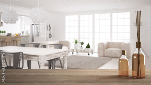 Wooden table top or shelf with aromatic sticks bottles over blurred scandinavian living room with dining table and sofa  white architecture interior design