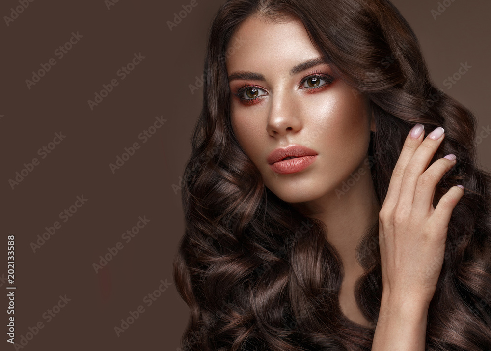 Beautiful brunette model with curls, classic makeup and full lips. The beauty of the face. Portrait shot in the studio.