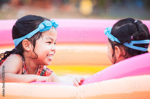 Two asian little child girls wearing swimming goggles playing water together in summer time with fun and happiness