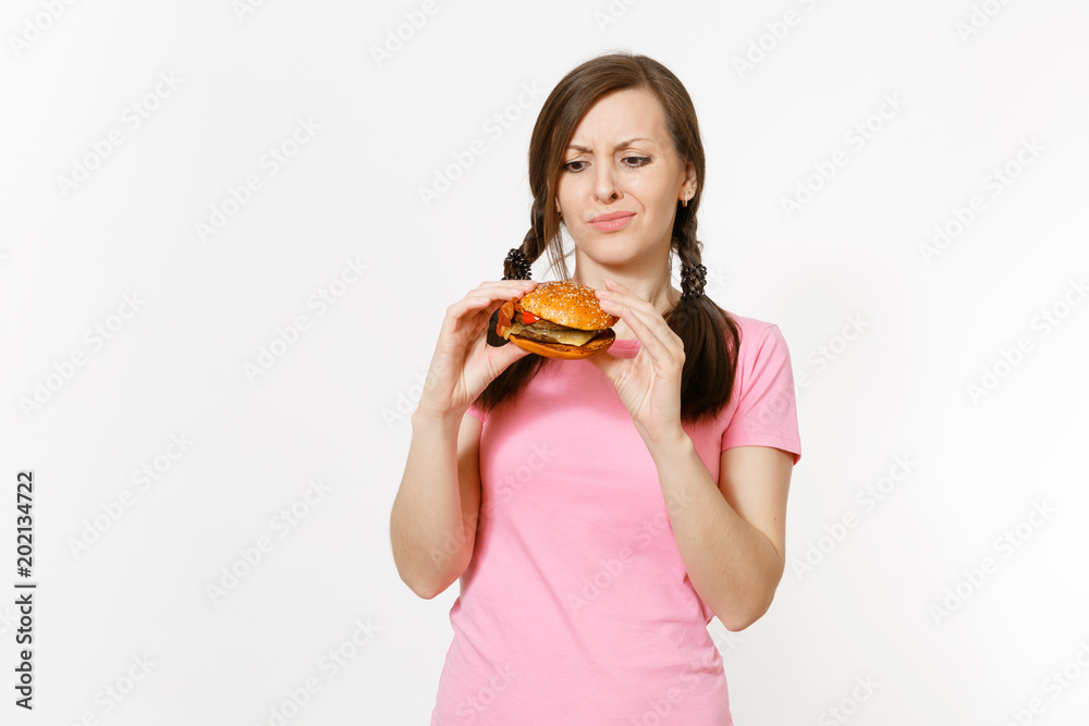 Young beautiful woman in pink t-shirt with braids holding in hands burger isolated on white background. Proper nutrition or American classic fast food. Copy space for advertisement. Advertising area. Young beautiful woman in pink t-shirt with braids holding in hands burger isolated on white background. Proper nutrition or American classic fast food. Copy space for advertisement. Advertising area.