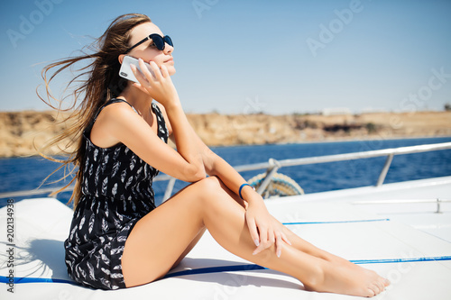 Young beautiful brunette girl talking on the phone while sitting on the yacht